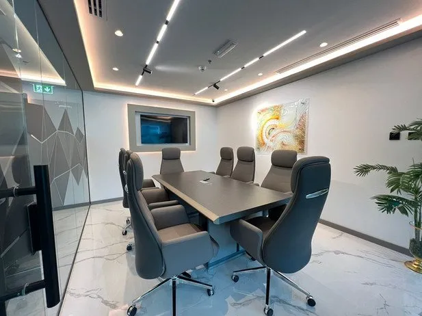 Conference room with large table, ergonomic chairs, and wall-mounted screen.