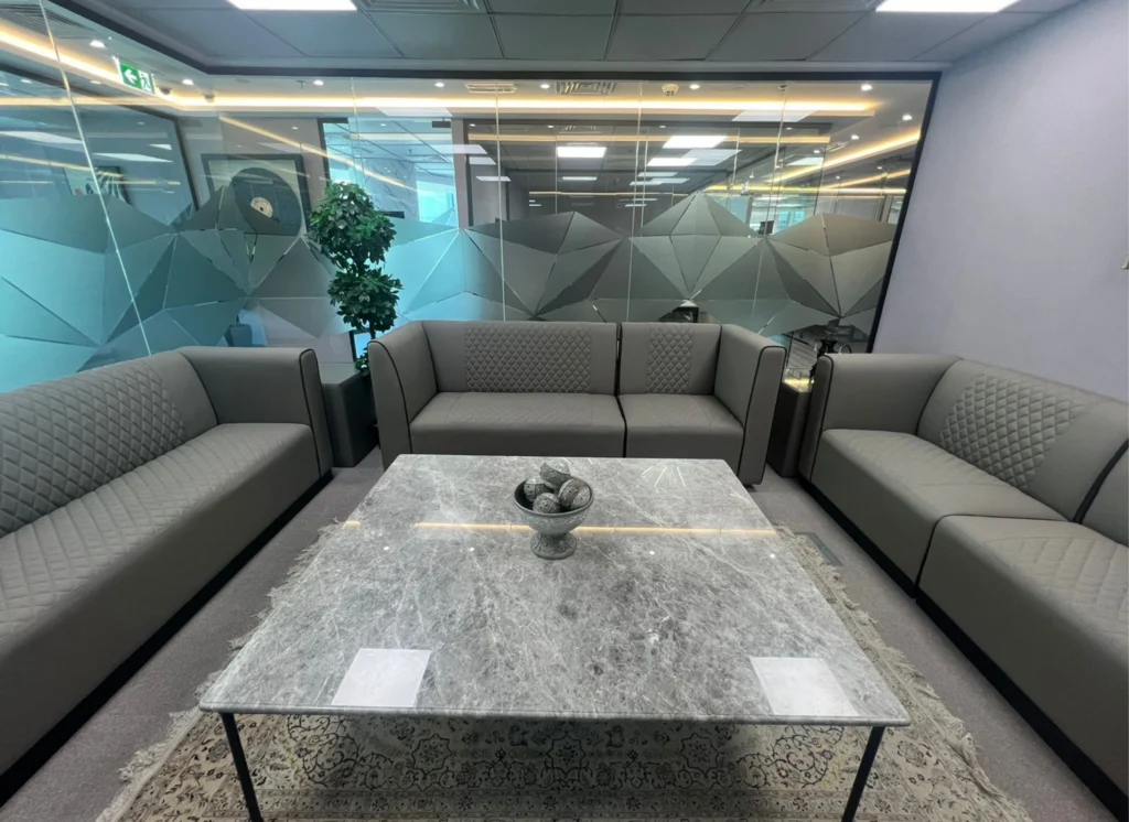 Symmetrical office lounge with quilted sofas and frosted glass wall.