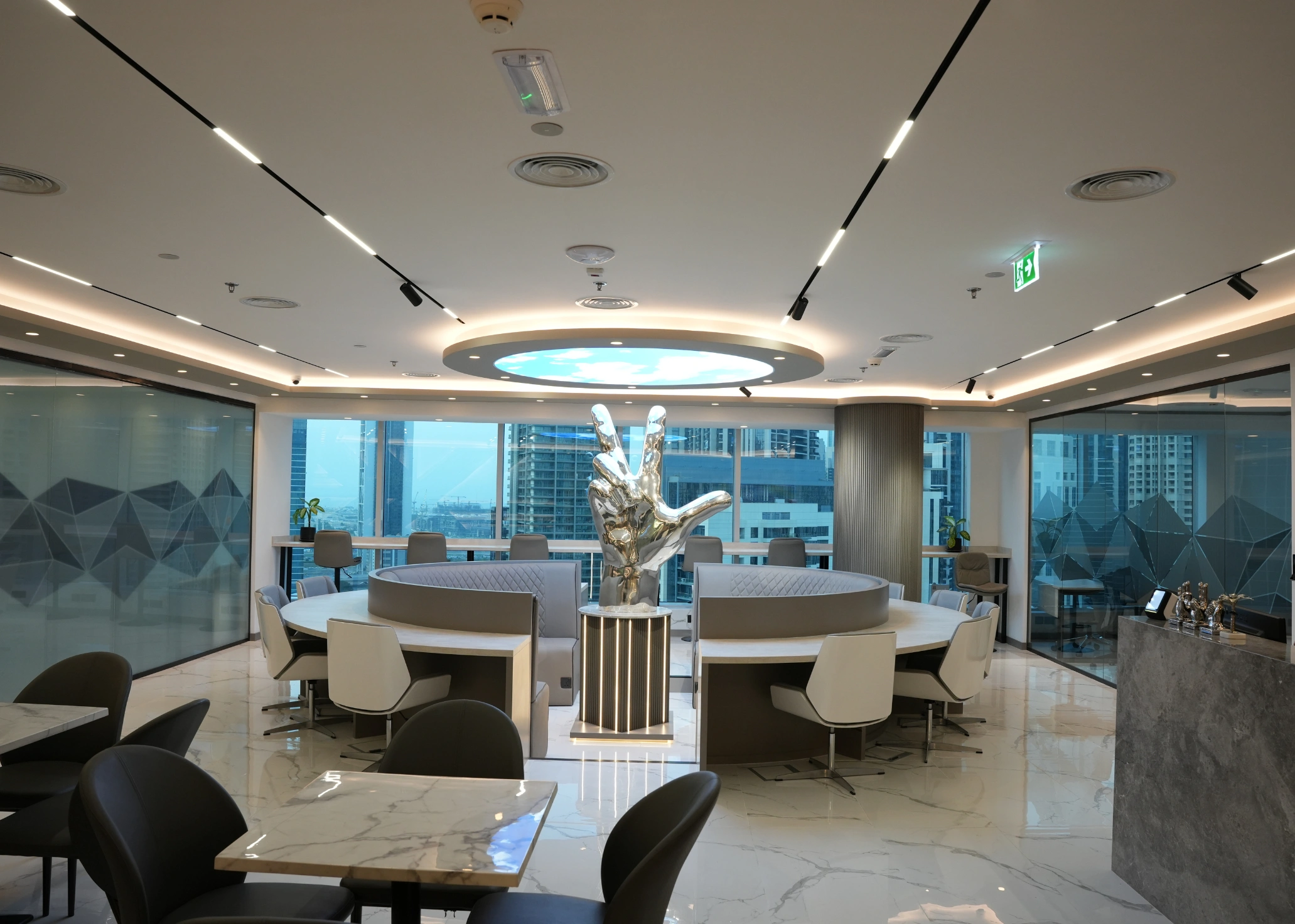 Modern office common area with a circular seating arrangement, silver peace sign sculpture, and city views.