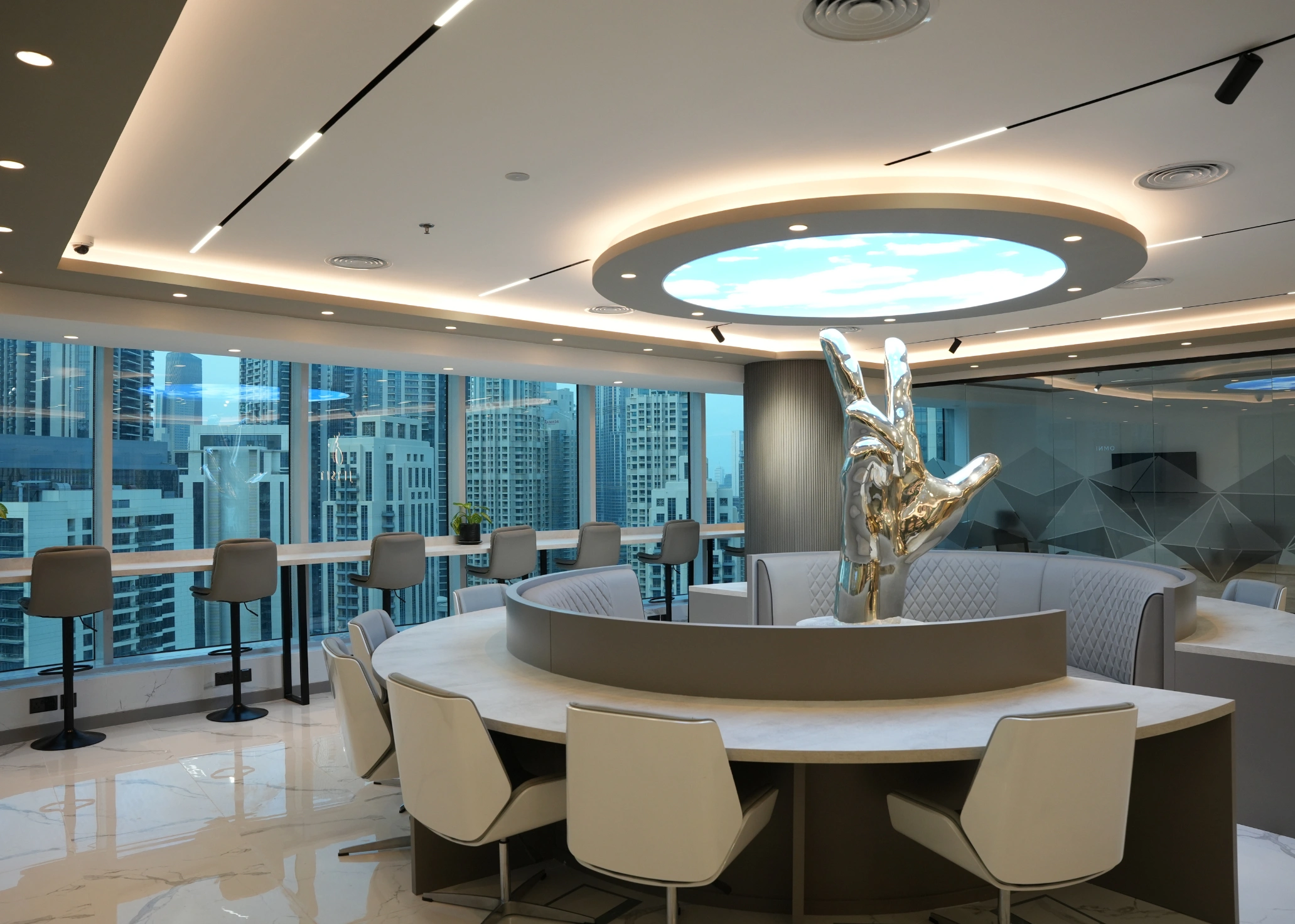 Wide view of a luxurious office lounge with a silver hand sculpture centerpiece and city views.